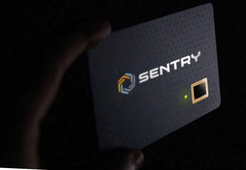 The Sentry Biometric Smart Card is presented with a hand holding it at an angle in a darkened setting. The green LED status light is on.